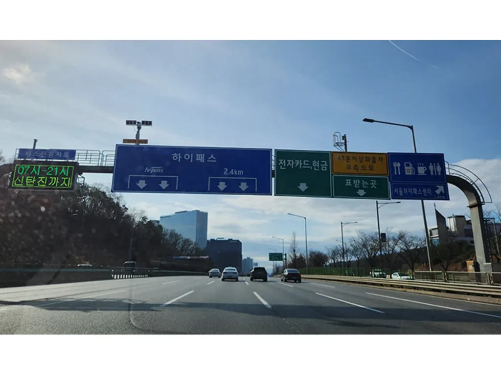 차량이 달리는 고속도로 위에 하이패스와 전자카드·현금 차로 안내판이 걸려 있다.